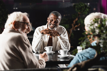 joyful african american man looking at blurred senior friends talking in bar