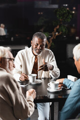 senior african american man gesturing during conversation with blurred friends in cafe