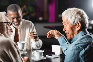 joyful senior multiethnic friends spending time together in cafe