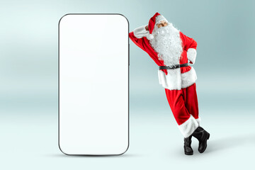 Smartphone mockup image, environment to showcase mobile app design, creative background. Smartphone for your advertising. Santa claus is standing next to a large smartphone. Christmas advertisement.