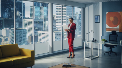 Successful Caucasian Businesswoman Using Laptop While Standing in Office Looking out of Window on Big City. Perfect Confident Female Digital Entrepreneur Developing e-Commerce Software Strategy.