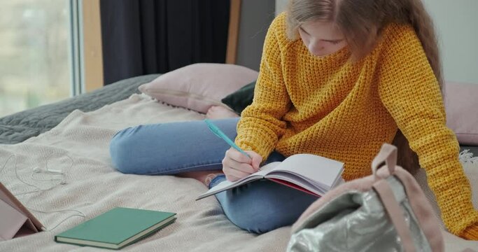  10 Year Old Girl Writing Something In Her Notebook, She Is Sitting On Her Bed In The Relaxation Room
