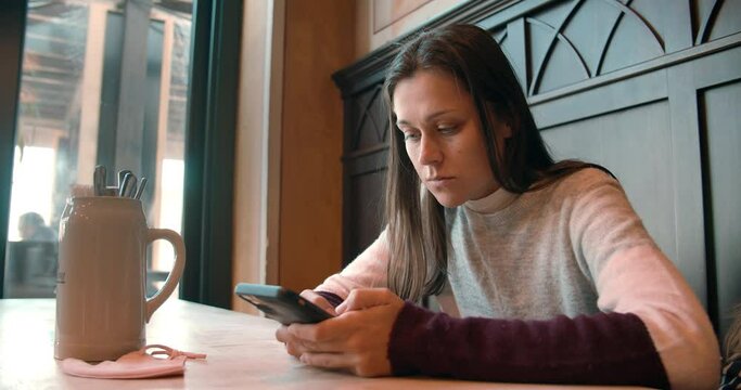 Young happy attractive woman in restaurant watching menu online using QR code with mobile phone choosing food plates for dinner lunch event dating 