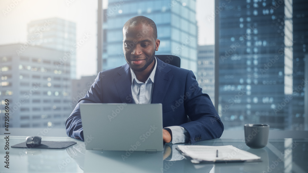 Poster successful black businessman in tailored suit working on laptop computer on top floor office overloo