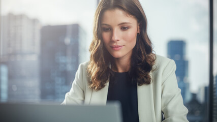 Portrait of Successful Young Businesswoman Sitting at Her Desk Working on Laptop Computer in Big...