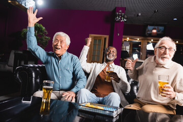cheerful senior multiethnic friends watching football championship in pub and showing win gesture