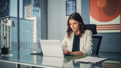 Portrait of Young Successful Caucasian Businesswoman Sitting at Desk Working on Laptop Computer in...
