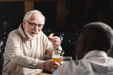 happy senior man clinking beer glasses with blurred african american friend