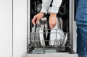 Woman doing dishes in dishwasher at home. Clean plates after washing modern kitchen with dishwashing machine. Household chores. 