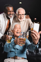 happy asian man taking selfie with senior multicultural friends in beer pub