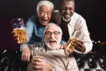 elderly friends with glasses of beer laughing at camera in pub
