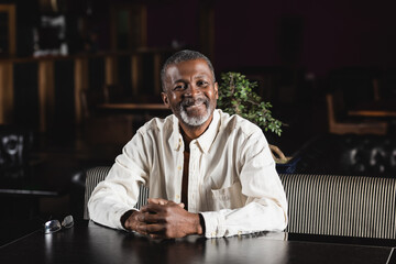 cheerful senior african american man sitting in pub and looking at camera