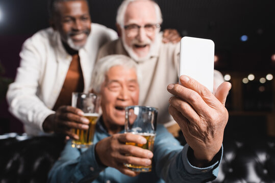 blurred asian man taking selfie on mobile phone with senior friends in beer pub