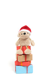 Small teddy bear in a Santa Claus hat sits on boxes with Christmas gifts.On a white background.