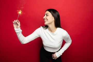 Holiday mood - smiling young woman in a white sweater holding sparklers
