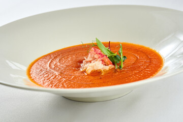Cream soup from baked tomato with crab in a white plate on a white tablecloth