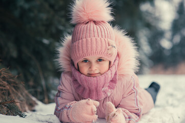 Close-up portrait of a happy girl in pink warm clothes in a winter fir forest