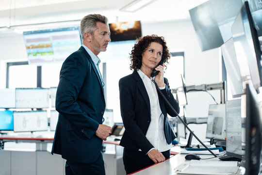 Businesswoman talking on telephone while standing with colleague in control room