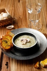 Mushroom Creamy Soup with Crispy Garlic Bread Baguette, Serve on Black Ceramic Bowl or Ramequin, on Rustic Brown Wooden Table.