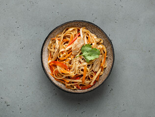 Asian food, wok noodle with vegetables and chicken in ceramic bowl, top view