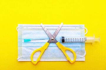 Needle scissors and a medical mask lie on a yellow background shown from top to bottom concept. covid 19.without vaccination