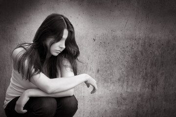 Monochrome outdoor photo of a sad anonymous girl thoughtful about troubles in front of a gray wall