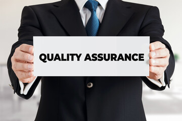 Businessman shows a banner with the message quality assurance. Business product or service quality guarantee