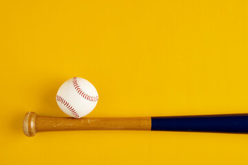 Wooden baseball bat and a ball on yellow background