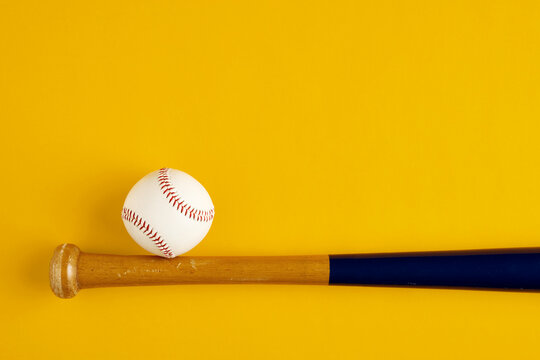 Wooden baseball bat and a ball on yellow background