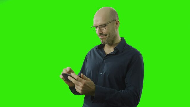 man with glasses is swiping on his phone and seams to be satisfied in front of a greenscreen
