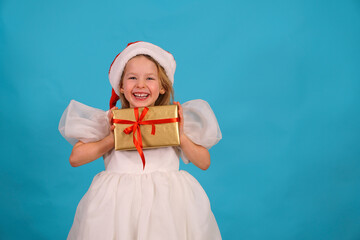 Happy little girl in a lush blom dress for a holiday. fun child in Santa hat hold gift Happy merry Christmas. beautiful girl smiles laughs. box gold bow. Happy New Year. Place for text. Copy space. 