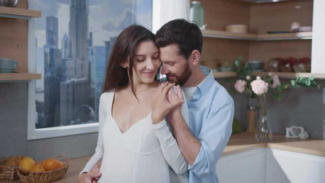 Caucasian attractive happy smiling couple of bearded young father husband with beautiful pregnant wife in kitchen. Relationship goals. Healthy planned pregnancy.