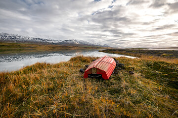 A red rowing boat laying on the green grass next to an icelandic fjord