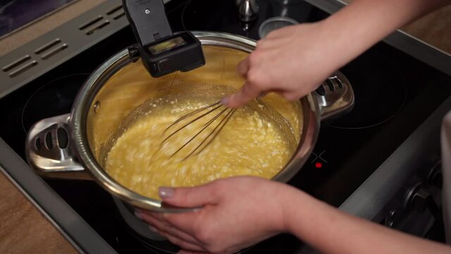 A professional blogger confectionery manufacturer kneads Christmas cake dough with a whisk. Step-by-step recipe for cooking cake in a pan on an induction cooker. Recording on an action camera