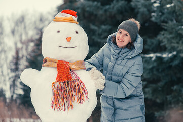 Woman sculpts a snowman in the winter snowy forest