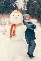 Cute girl and happy snowman in knitted hat and scarf