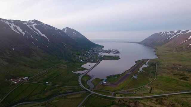 Aerial shot approaching town in Icelandic fjord. Beautiful scenery with snowy mountains.