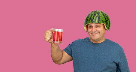 guy in a watermelon helmet holds a glass of red juice in his hands