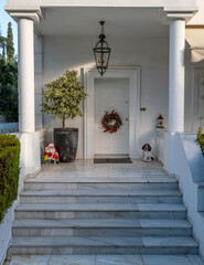 Christmas wreath, Santa and dog decorated house entrance with white door, columns and marble stairs.
