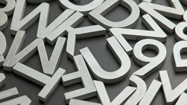 full frame close-up looped rotating background of silver metal letters on flat black surface
