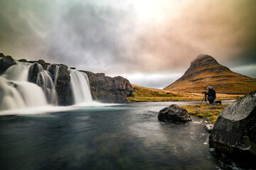 Kirkjufellsfoss Iceland long exposure with dramatic sky and fotographer kneeing to take picture