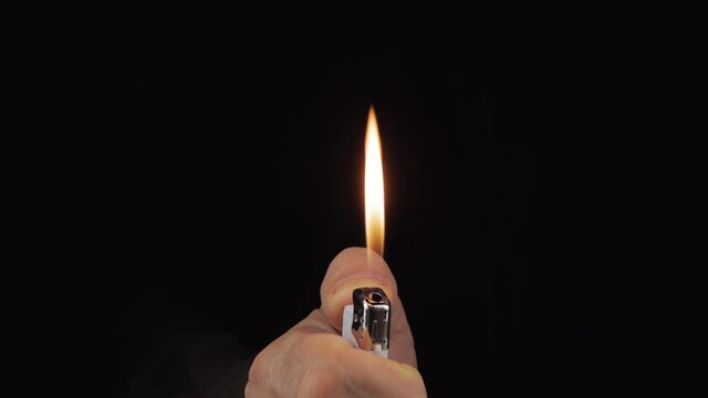 A man's hand with a gas lighter in the dark. A man makes a fire.