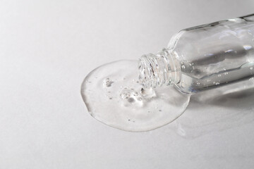Transparent facial serum with hyaluronic acid pouring from glass bottle on grey background. Cosmetic product with collagen closeup. Beauty concept.