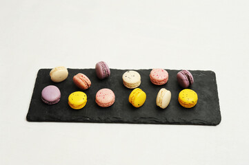 Colorful french macarons on black slate board, white background