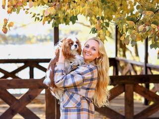 girl in a plaid shirt in autumn in the park with a dog cavalier king charles spaniel
