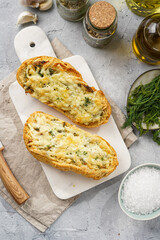 Two halves of garlic and butter bread - baguette on a marble board, sea salt, pepper, dill and garlic cloves on a grey concrete background, top view