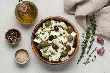 Soft feta cheese with olive oil, herbs and olives in wooden bowl on white background. Pieces of marinated cheese with fresh thyme