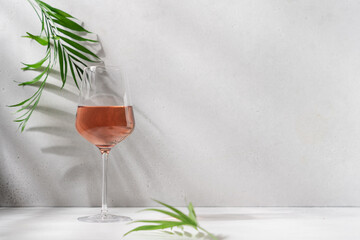 Rose wine in an elegant glass on white background with shadows and palm leaves. Romantic party, vacation, holiday concept