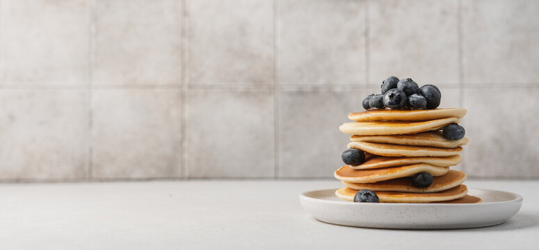 Homemade pancakes with blueberries in stack on light table with tile background