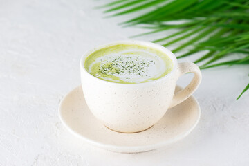 Matcha latte tea with coconut milk and hemp seeds in a mug on the background of a palm branch.